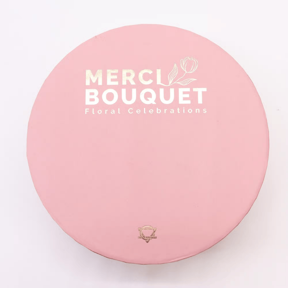 Pink round container with 'Merci Bouquet' branding on a light pink background