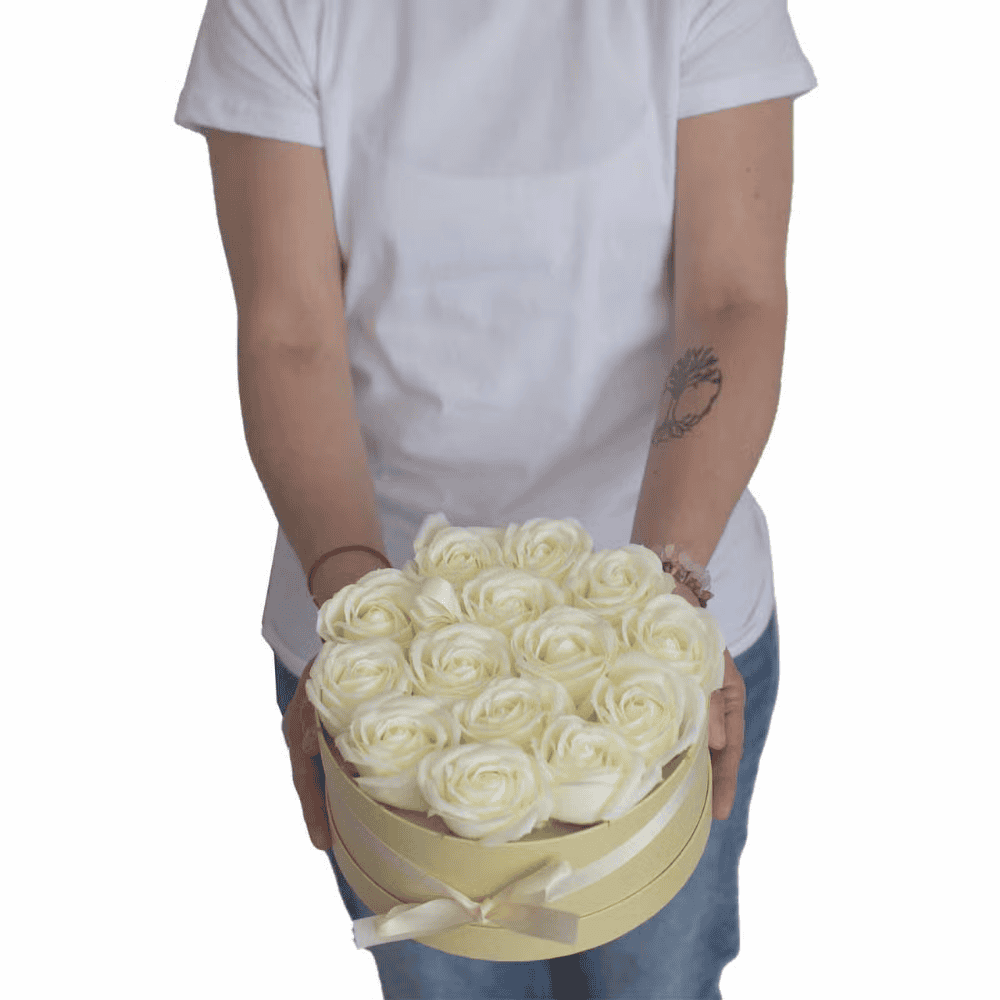 Person holding a round box of white soap roses against a white background