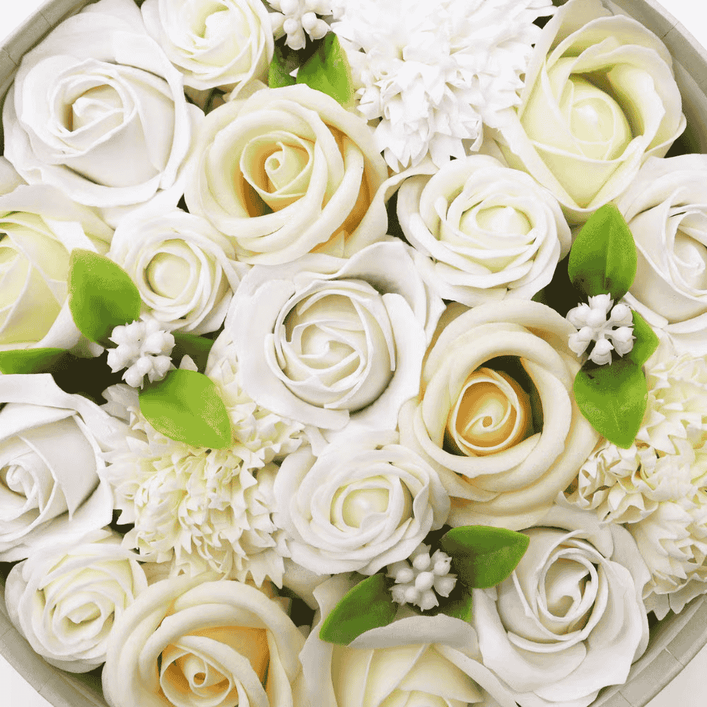 Close-up of white and yellow soap roses with green leaves in a box.