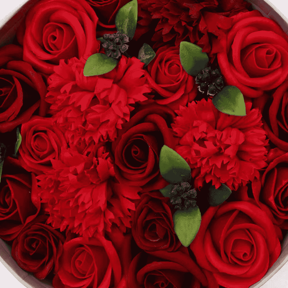 Close-up of red soap roses and red carnations with green leaves in a circular arrangement.