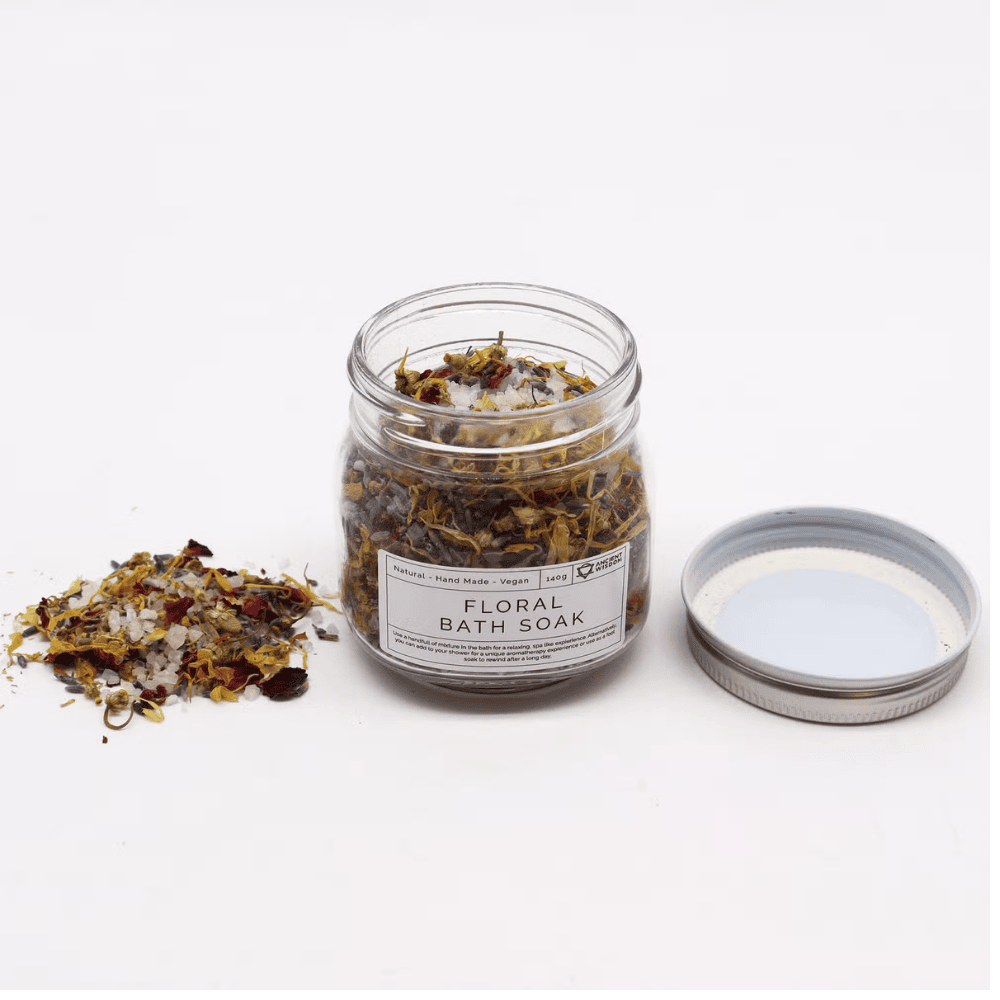 Jar of floral bath soak with scattered ingredients on a white background