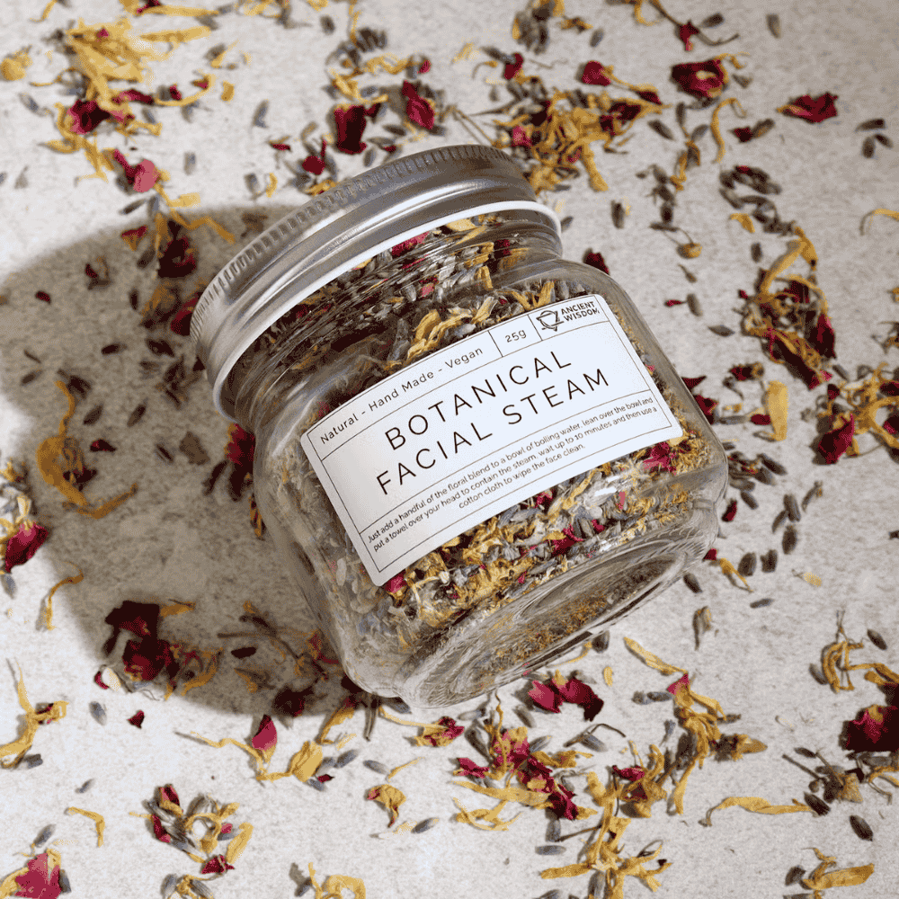 Jar of botanical facial steam with a label on a surface with dried flowers.