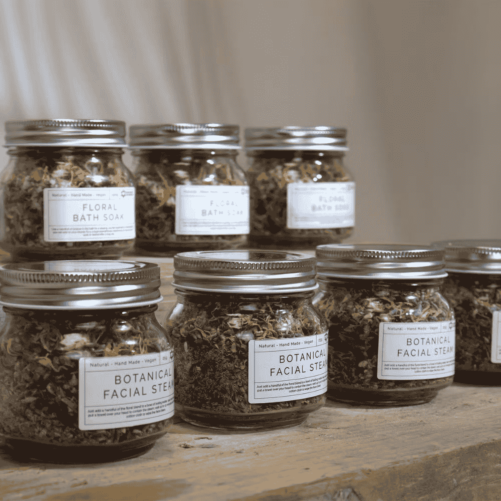 Jars of botanical facial steams on a wooden surface with a neutral background
