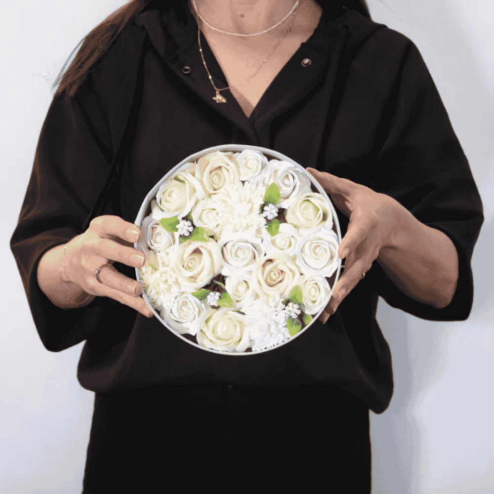 Person holding a round box of white soap roses against a plain background